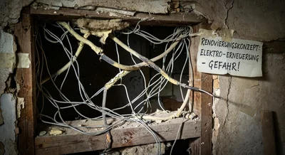 Nahaufnahme einer alten, schadhaften Elektroinstallation mit verfärbten Kabeln und korrodierten Metallteilen in einem Stromkasten