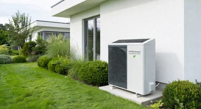 Vergleich einer modernen Wärmepumpen-Außeneinheit mit einer älteren Elektroheizung an einer Hauswand